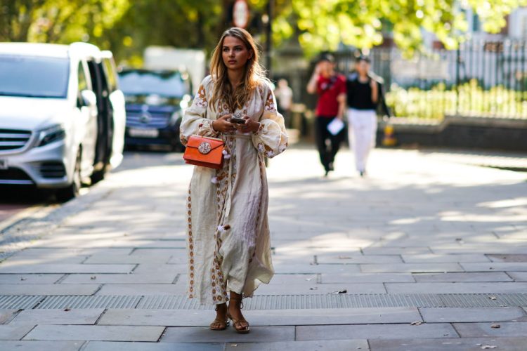 LONDON, ENGLAND - SEPTEMBER 15: A guest wears a white long dress with brown pixel geometric patterns, an orange leather bag, sandals, during London Fashion Week September 2019 on September 15, 2019 in London, England. (Photo by Edward Berthelot/Getty Images)