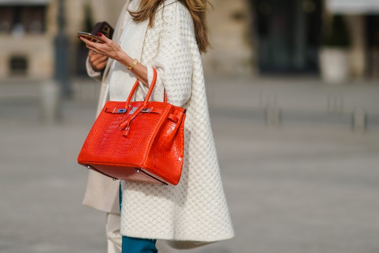 PARIS, FRANCE - FEBRUARY 06: A passerby wears a white knitted long jacket, an orange leather crocodile pattern Hermes Birkin bag, a golden bracelet, blue jeans, on February 06, 2021 in Paris, France. (Photo by Edward Berthelot/Getty Images)