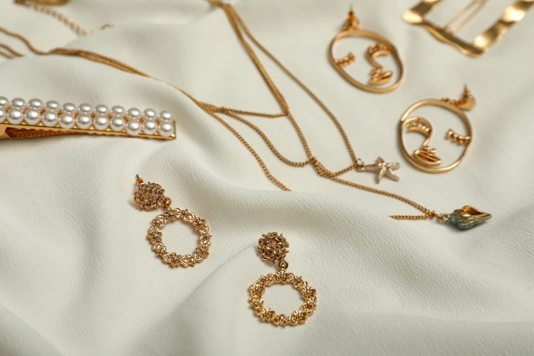 Stylish golden bijouterie on white fabric. Elegant jewelry